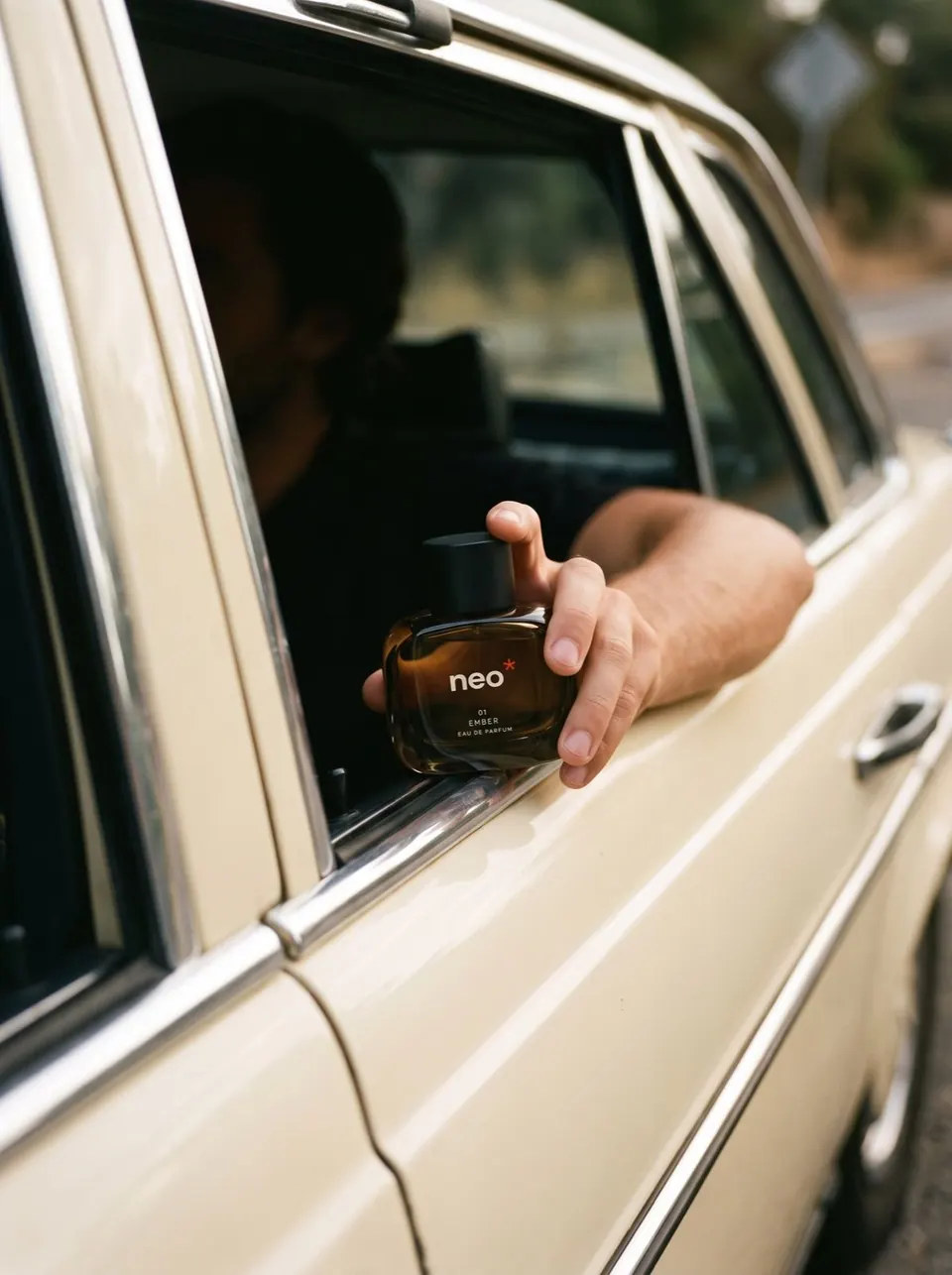Main tenant un flacon de parfum NEO par la fenêtre d’une voiture ancienne crème