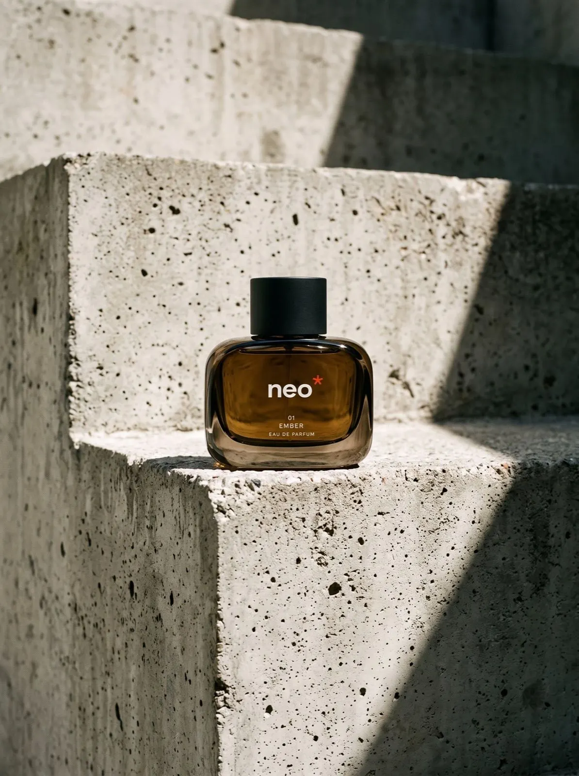 Flacon de parfum NEO Ember posé sur une marche en béton brut, en plein soleil