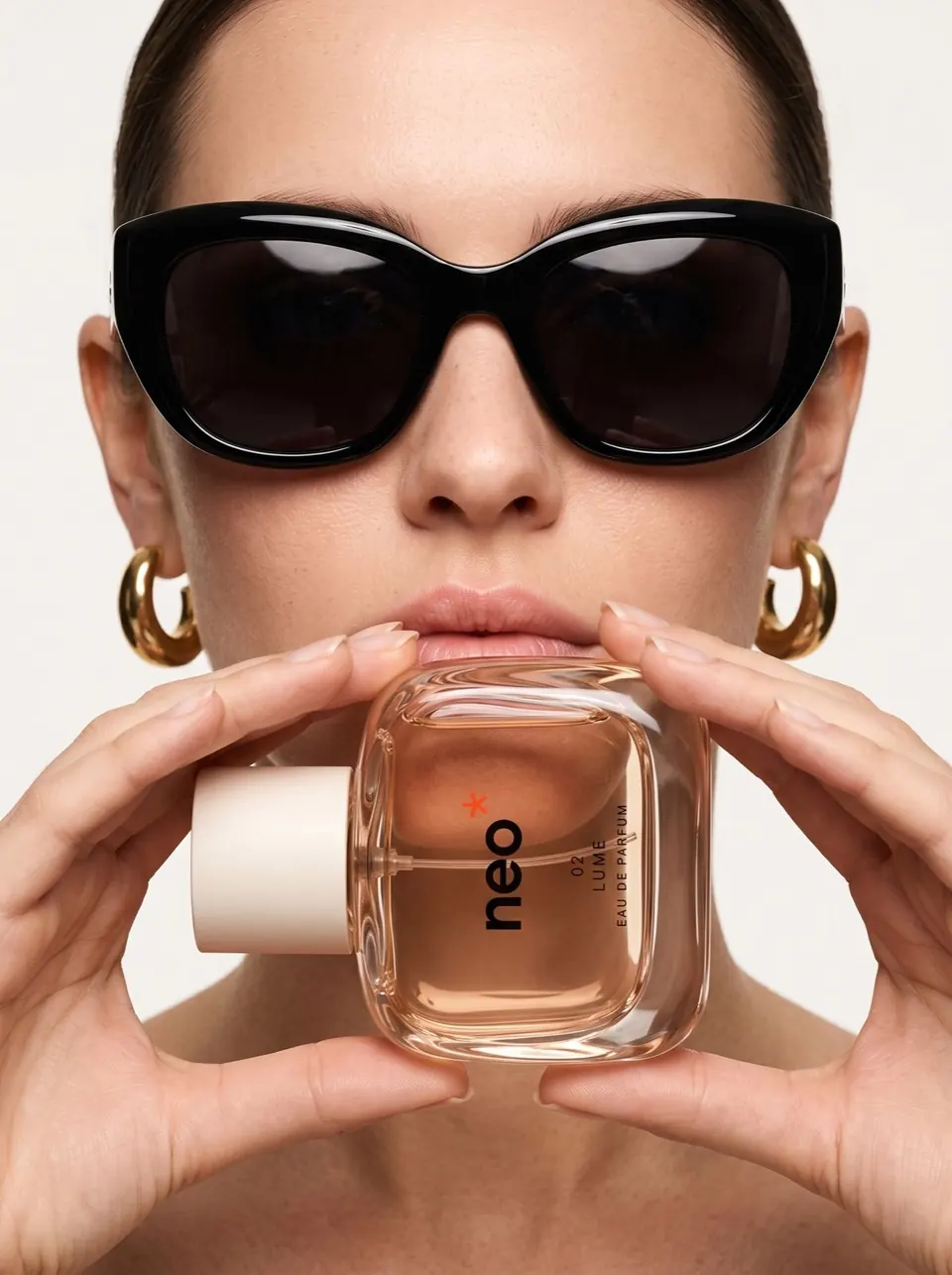 Femme en lunettes de soleil tenant un flacon de parfum NEO devant sa bouche, en studio