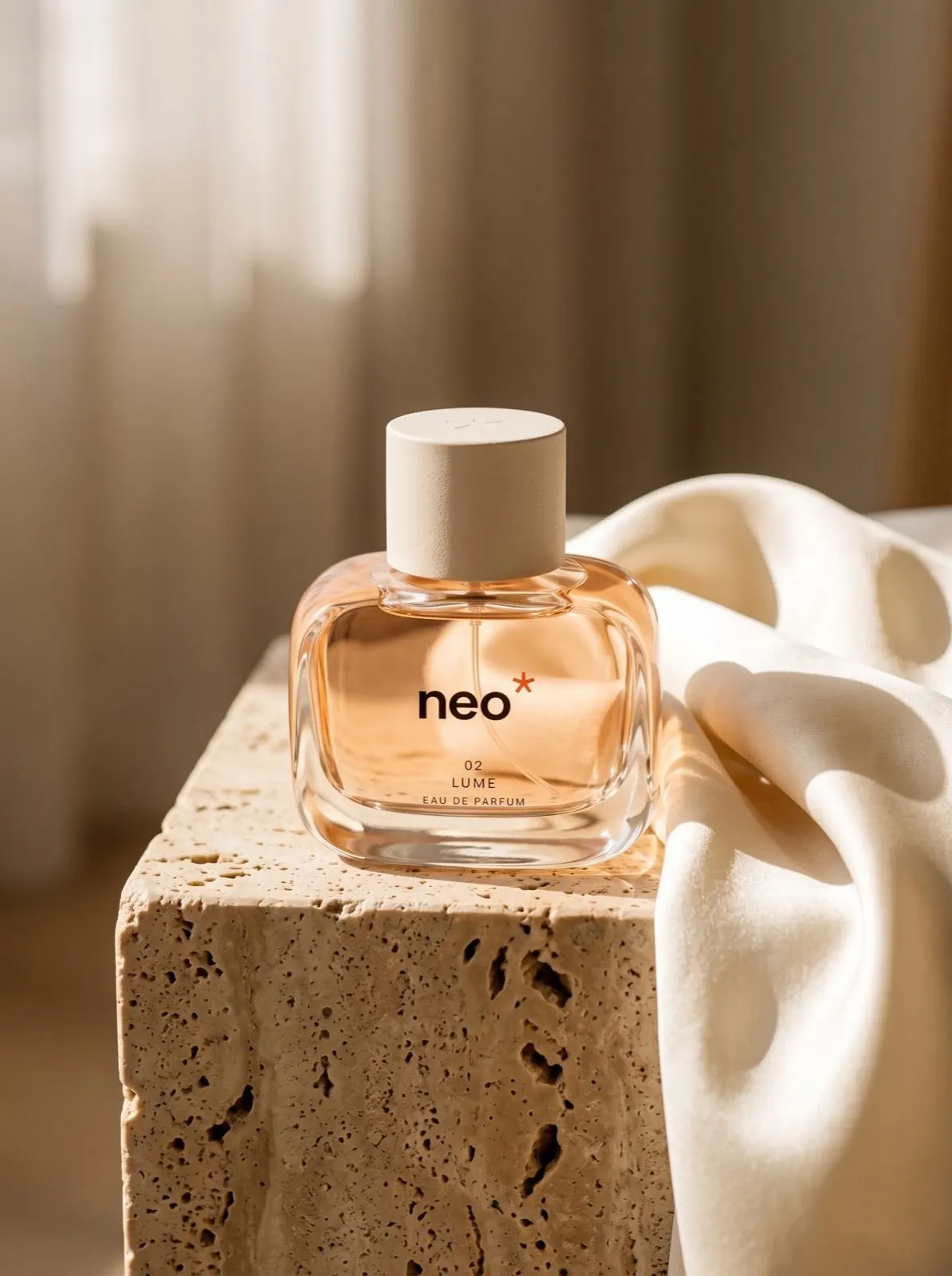 Flacon de parfum NEO posé sur un bloc de travertin, à côté d’un tissu crème